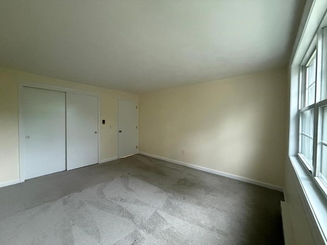 unfurnished bedroom with carpet, baseboards, a closet, and multiple windows