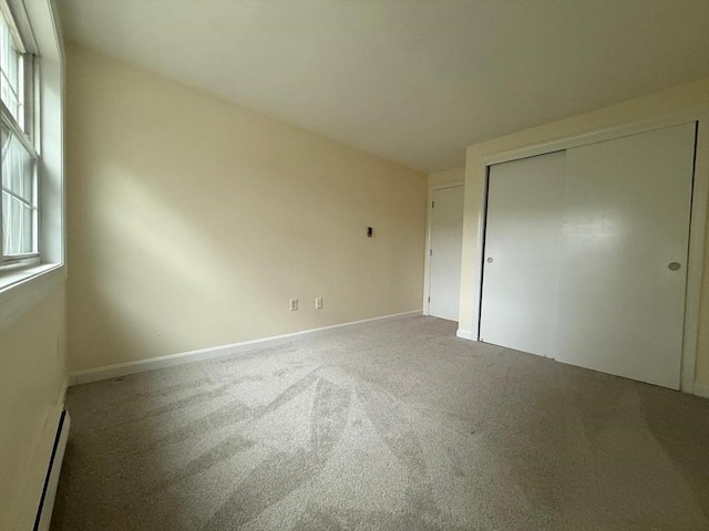 unfurnished bedroom with baseboards, a baseboard radiator, a closet, and carpet