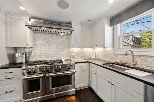 kitchen with double oven range, wall chimney exhaust hood, a sink, backsplash, and dark countertops