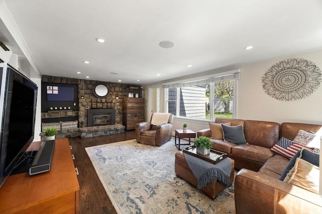 living room with wood finished floors, a stone fireplace, ornamental molding, and recessed lighting