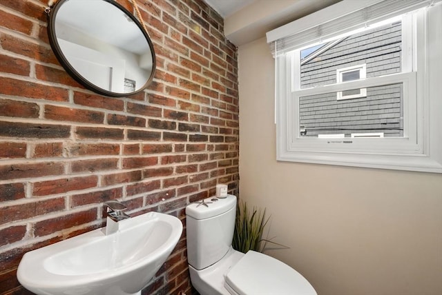 half bathroom with a sink, brick wall, and toilet