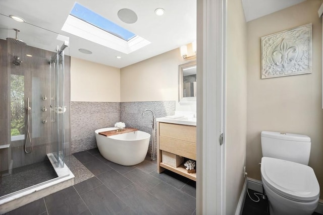 bathroom with a skylight, toilet, a stall shower, vanity, and a freestanding tub
