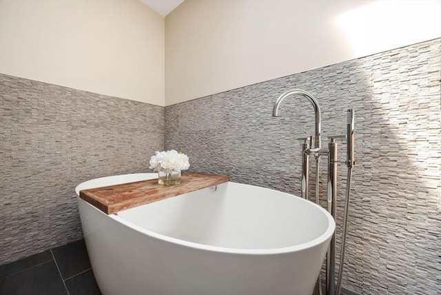 full bathroom with tile walls, tile patterned flooring, a freestanding bath, a sink, and wainscoting