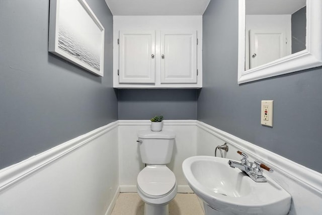 half bathroom with a sink, toilet, and wainscoting