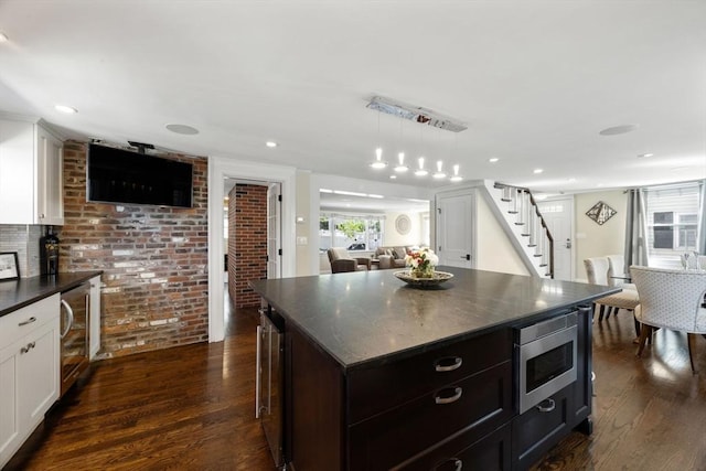 kitchen featuring stainless steel microwave, beverage cooler, dark wood finished floors, brick wall, and white cabinets