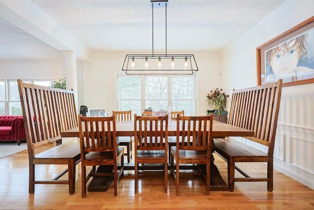 dining area featuring ornate columns, light wood-style flooring, and crown molding