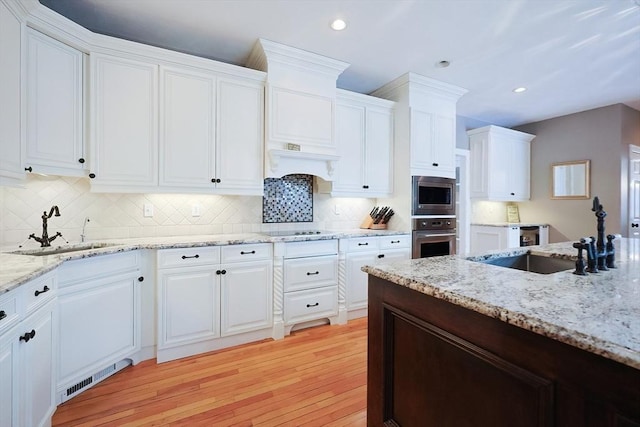 kitchen with tasteful backsplash, appliances with stainless steel finishes, light wood-type flooring, white cabinetry, and a sink