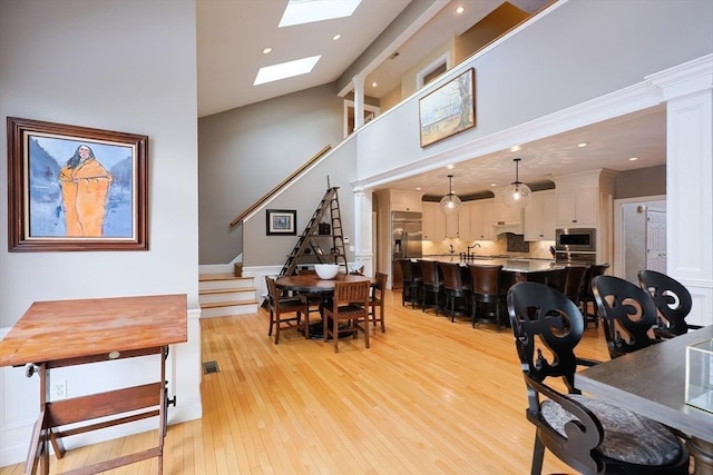 dining space with a skylight, visible vents, a towering ceiling, stairs, and light wood-type flooring