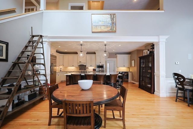 dining space featuring light wood finished floors, a high ceiling, and recessed lighting