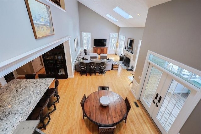 living area with a skylight, visible vents, light wood-style flooring, a fireplace, and high vaulted ceiling