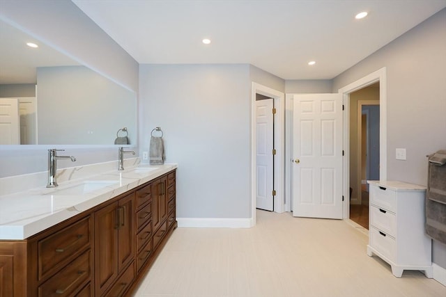 bathroom with baseboards, double vanity, a sink, and recessed lighting