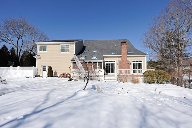 snow covered rear of property featuring fence, a chimney, and a wooden deck