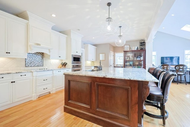 kitchen featuring a kitchen island with sink, appliances with stainless steel finishes, white cabinetry, and decorative light fixtures