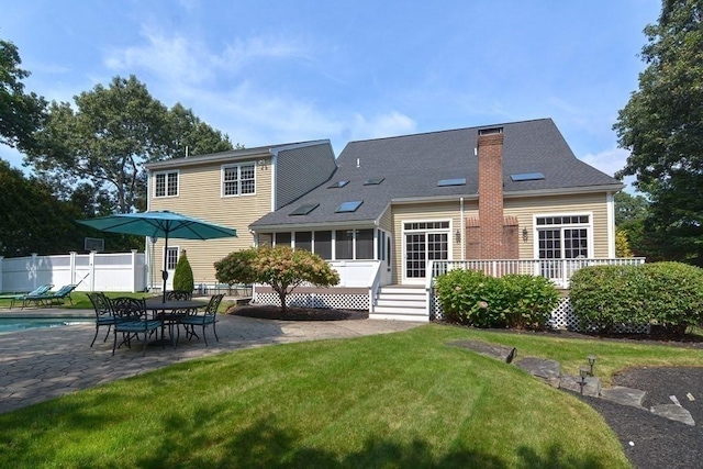 back of property with a yard, a chimney, a patio, a sunroom, and fence