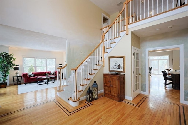 staircase featuring a towering ceiling, baseboards, and wood finished floors