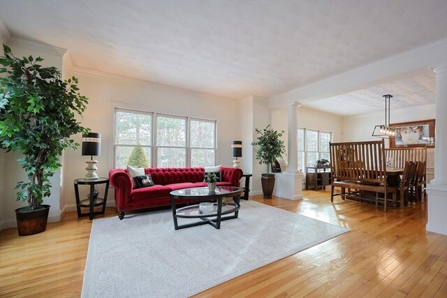 living area featuring a chandelier, light wood-style flooring, baseboards, ornamental molding, and ornate columns