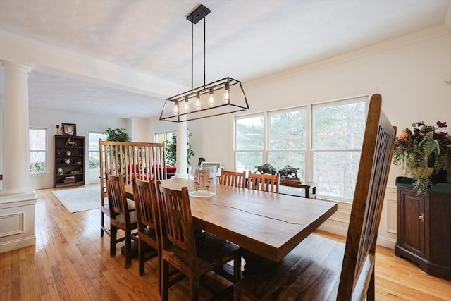 dining area featuring a wealth of natural light, crown molding, light wood finished floors, and ornate columns