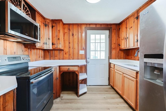 kitchen with sink, light hardwood / wood-style flooring, stainless steel appliances, and wood walls