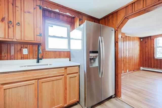 kitchen with sink, wood walls, stainless steel refrigerator with ice dispenser, a baseboard radiator, and light wood-type flooring