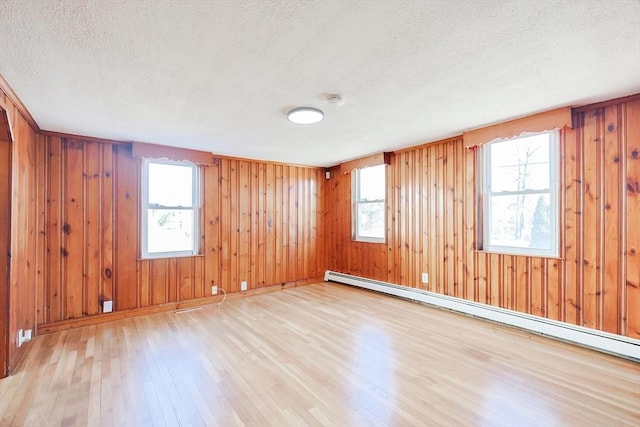 spare room featuring light hardwood / wood-style flooring, a baseboard radiator, a textured ceiling, and plenty of natural light