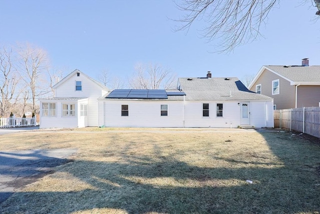 back of property with a lawn and solar panels