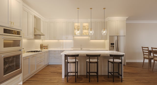 kitchen with a breakfast bar area, appliances with stainless steel finishes, range hood, a kitchen island, and decorative light fixtures