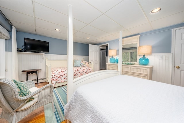 bedroom featuring wood-type flooring, a baseboard radiator, and a paneled ceiling