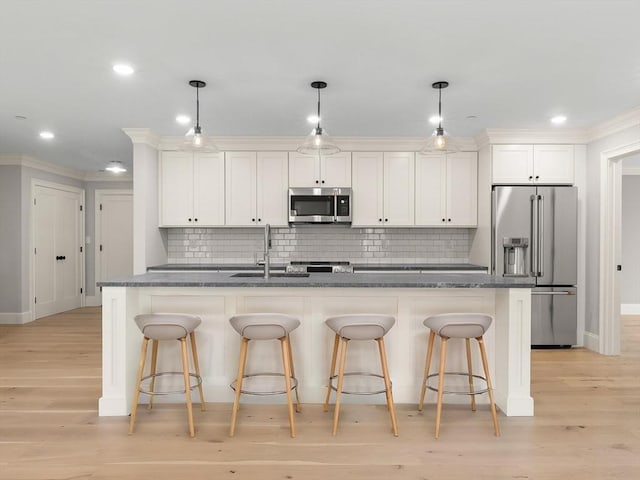 kitchen with a kitchen island with sink, appliances with stainless steel finishes, a sink, baseboards, and white cabinetry