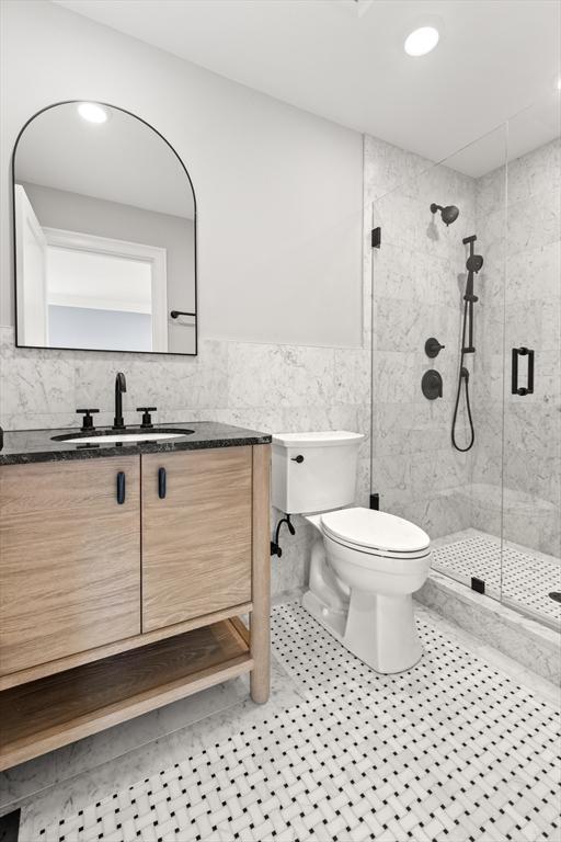bathroom with tile walls, a shower stall, vanity, tile patterned floors, and toilet