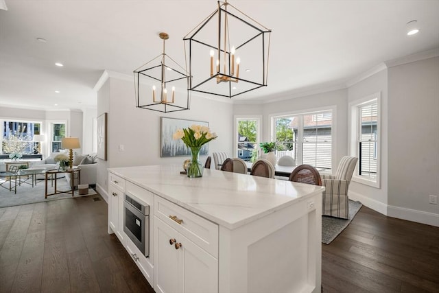 kitchen with ornamental molding, stainless steel microwave, a chandelier, dark wood-type flooring, and white cabinets