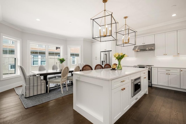 kitchen with under cabinet range hood, stainless steel appliances, crown molding, dark wood finished floors, and a chandelier
