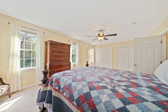 bedroom featuring light colored carpet, baseboards, two closets, and multiple windows