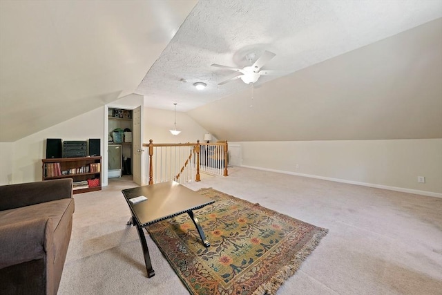 interior space featuring a ceiling fan, a textured ceiling, light colored carpet, baseboards, and lofted ceiling