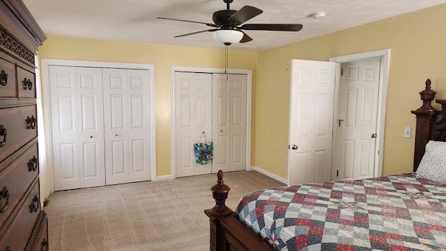 bedroom with a ceiling fan, multiple closets, light colored carpet, and baseboards
