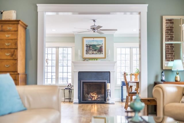 sitting room featuring ceiling fan, ornamental molding, a glass covered fireplace, and wood finished floors