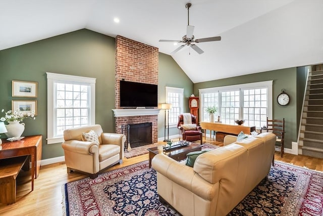 living room with stairs, a brick fireplace, ceiling fan, and plenty of natural light
