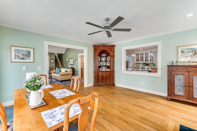 dining space featuring baseboards, ornamental molding, light wood finished floors, ceiling fan, and stairway