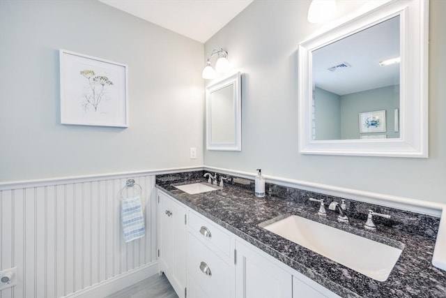 bathroom featuring a wainscoted wall, visible vents, a sink, and double vanity