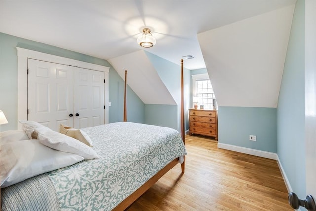 bedroom featuring a closet, light wood-type flooring, visible vents, baseboards, and vaulted ceiling