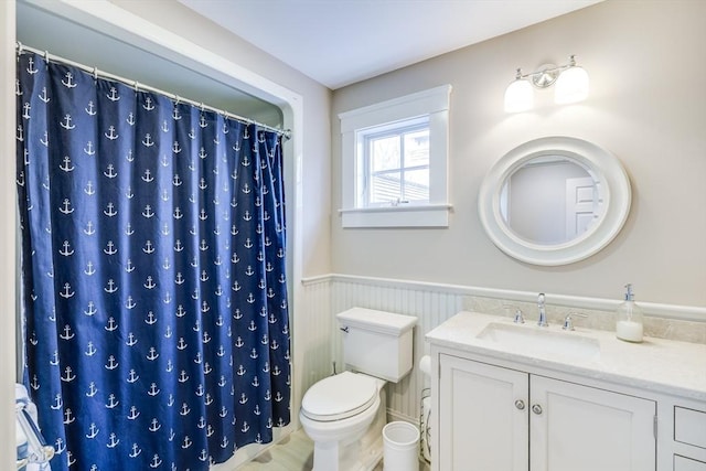 full bathroom featuring toilet, vanity, a wainscoted wall, and curtained shower