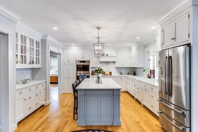 kitchen featuring stainless steel appliances, glass insert cabinets, light wood finished floors, light countertops, and white cabinets