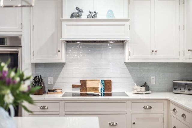 kitchen with backsplash, black electric cooktop, light countertops, and white cabinets