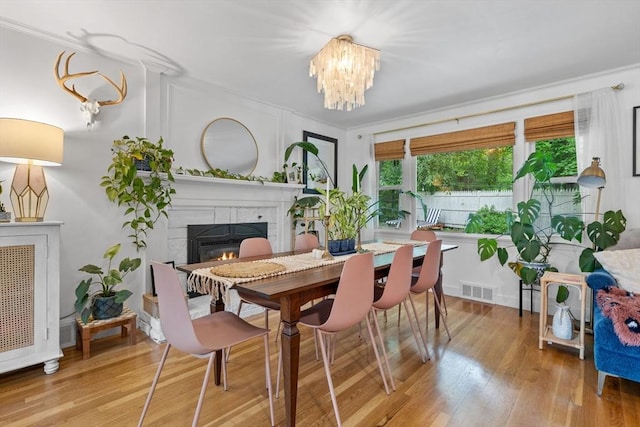 2313 Washington St, Holliston, MA 01746 - dining space with a tiled fireplace, light wood-style flooring, a chandelier, and crown molding
