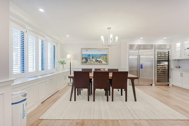 dining space featuring light hardwood / wood-style flooring, beverage cooler, crown molding, and a notable chandelier