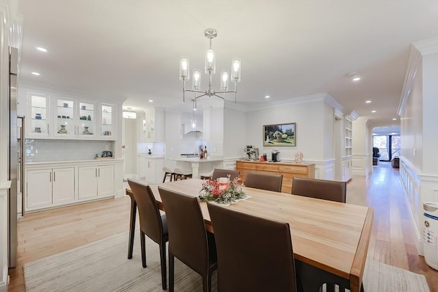 dining area with light wood-type flooring, crown molding, and a chandelier