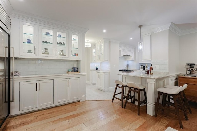 kitchen featuring light stone countertops, a kitchen breakfast bar, light hardwood / wood-style flooring, white cabinetry, and hanging light fixtures