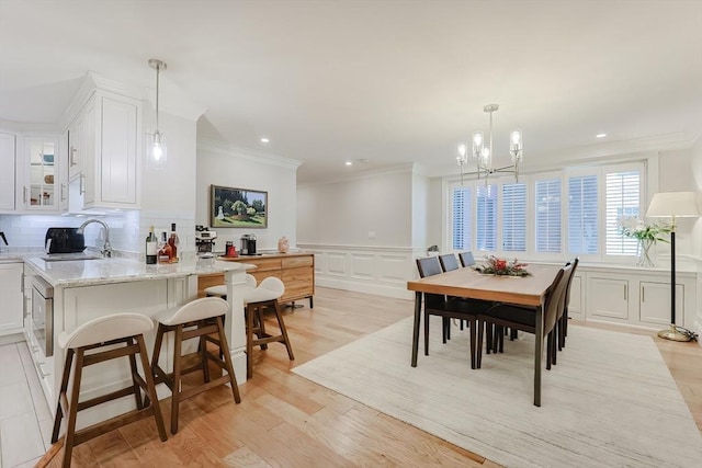 dining room with light hardwood / wood-style flooring, ornamental molding, sink, and an inviting chandelier