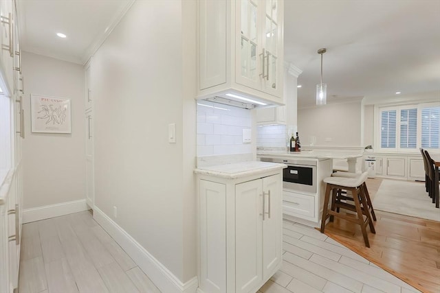 kitchen featuring pendant lighting, a breakfast bar, decorative backsplash, ornamental molding, and white cabinetry