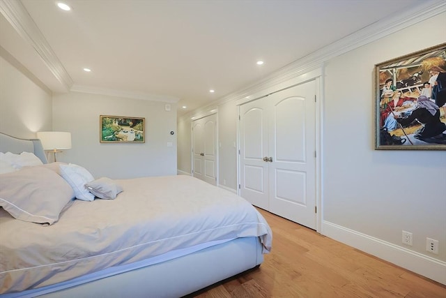 bedroom featuring light wood-type flooring, ornamental molding, and multiple closets