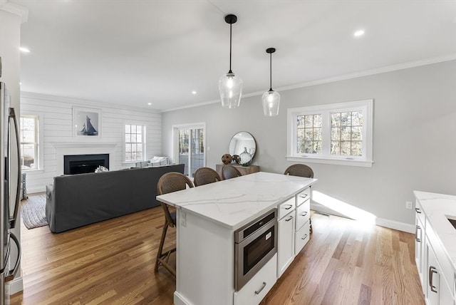 kitchen with a breakfast bar, a kitchen island, white cabinets, hanging light fixtures, and light stone countertops